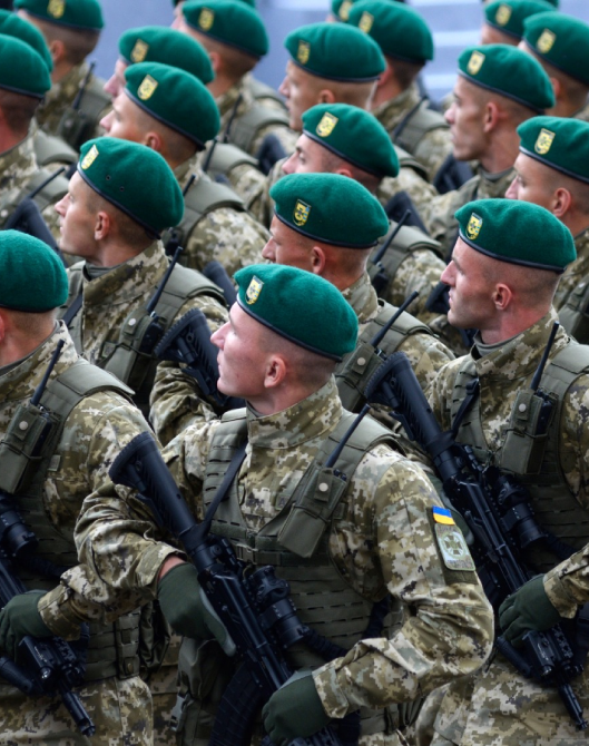 A soldier in camouflage tactical gear and a police officer in a navy duty uniform standing side by side
